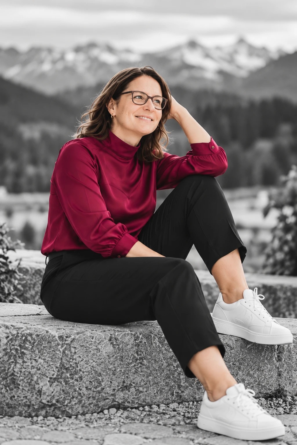 Bianka Bitter, Gründerin von Strukturreich, in Bluse in Himbeere auf einer Steinmauer vor den Bergen